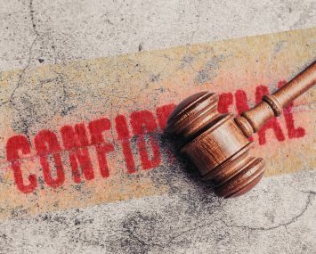 Wooden judge gavel on gray stone background with Confidential stamped behind it.