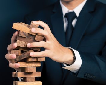 A man in a suit holding a falling Jenga tower.