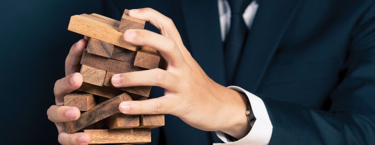 A man in a suit holding a falling Jenga tower.