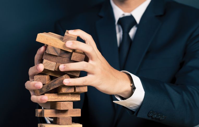 A man in a suit holding a falling Jenga tower.