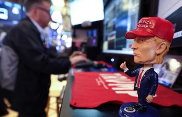 A bobble head depicting President Donald Trump sits on a desk as traders works on the floor of the New York Stock Exchange.