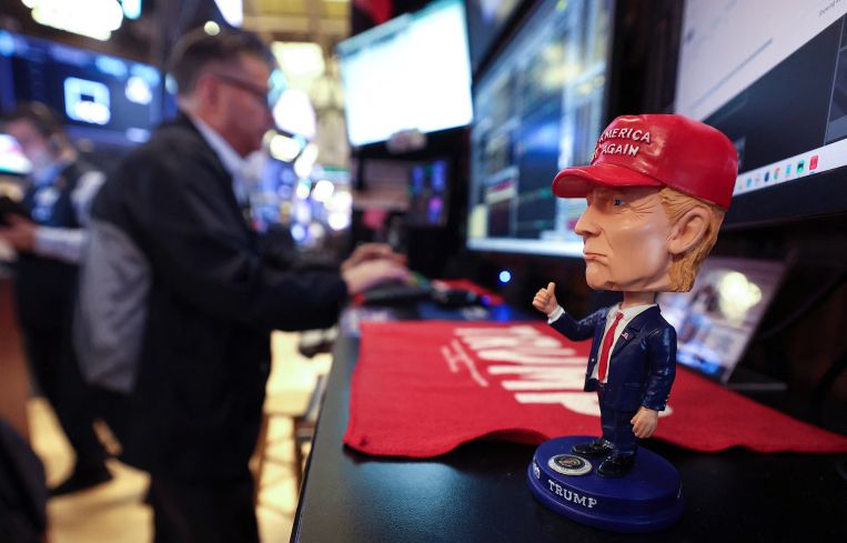 A bobble head depicting President Donald Trump sits on a desk as traders works on the floor of the New York Stock Exchange.