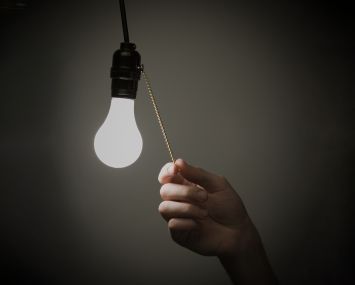 A hand pulling on a chain to turn off a lightbulb next to the chain.