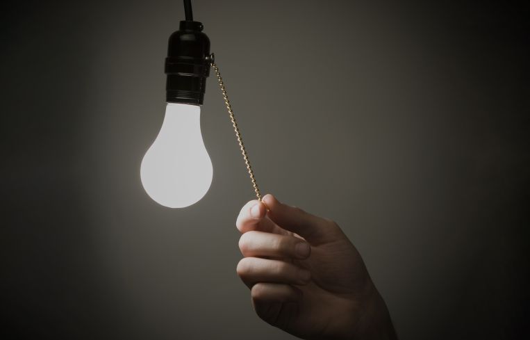 A hand pulling on a chain to turn off a lightbulb next to the chain.