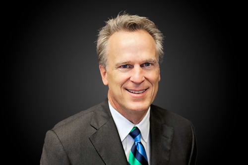 Headshot of a man in a suit, smiling.