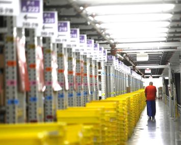 A worker transports plastic crates filled with orders at a distribution center.