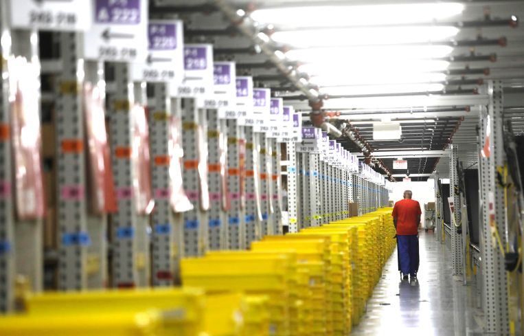 A worker transports plastic crates filled with orders at a distribution center.