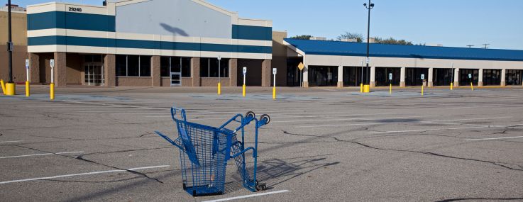 A shopping cart lies in a parking lot at a mostly-vacant shopping center.