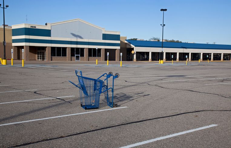 A shopping cart lies in a parking lot at a mostly-vacant shopping center.