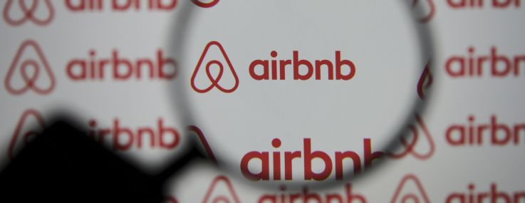A magnifier is seen in front of a screen displaying the Airbnb logo.