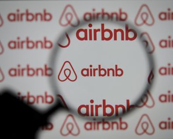 A magnifier is seen in front of a screen displaying the Airbnb logo.