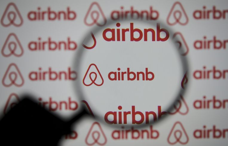 A magnifier is seen in front of a screen displaying the Airbnb logo.