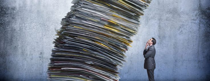 An illustration of a businessman looks up as a large stack of paperwork is leaning towards him.