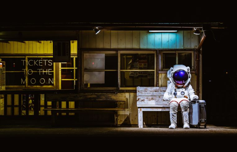 A person in a space suit sitting at a train station with a suitcase.