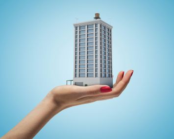 Female hand holding high building on blue background. Home and mortgage. Digital art. Building and construction.
