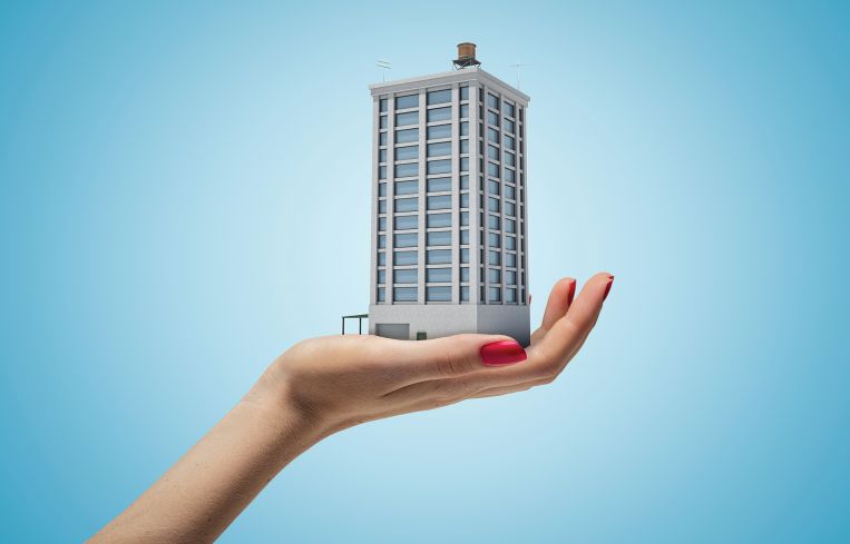 Female hand holding high building on blue background. Home and mortgage. Digital art. Building and construction.