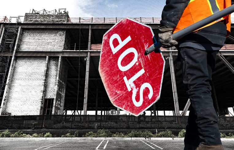 A construction site with someone holding a big stop sign in front of it.