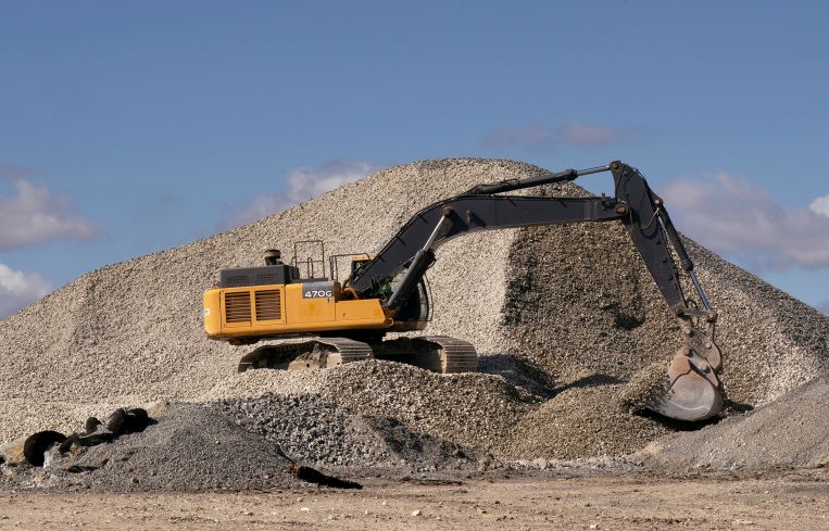 An excavator scoops rocks from a pile.