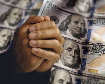 Clasped, begging hands in front of hundred dollar bills.