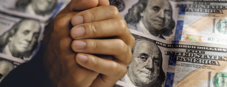 Clasped, begging hands in front of hundred dollar bills.