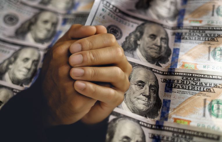 Clasped, begging hands in front of hundred dollar bills.