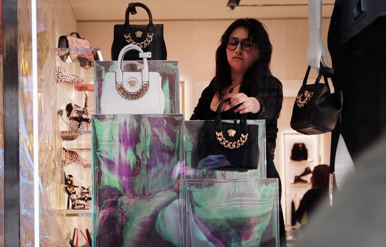 A woman takes down luxury handbags in a windows display in SoHo.