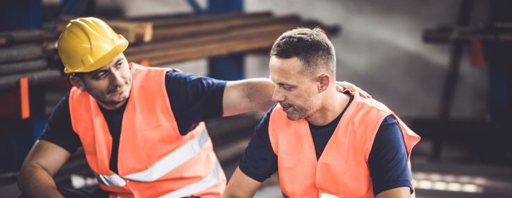 Sad manual worker being consoled by his colleague in aluminum mill.