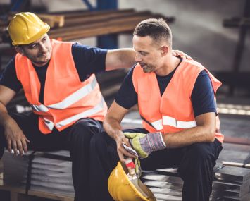 Sad manual worker being consoled by his colleague in aluminum mill.