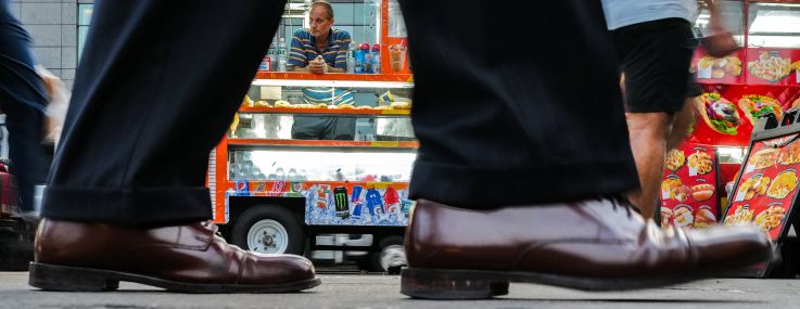 A hot dog and snack vendor in Manhattan waits for customers while pedestrians walk by.
