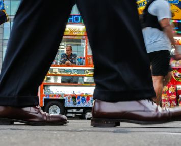 A hot dog and snack vendor in Manhattan waits for customers while pedestrians walk by.