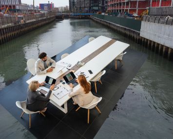 A group of office workers at a table floating in the Gowanus Canal.