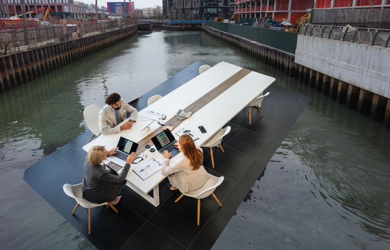 A group of office workers at a table floating in the Gowanus Canal.