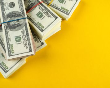 Stacks of US dollars in bundles on a bright yellow background.