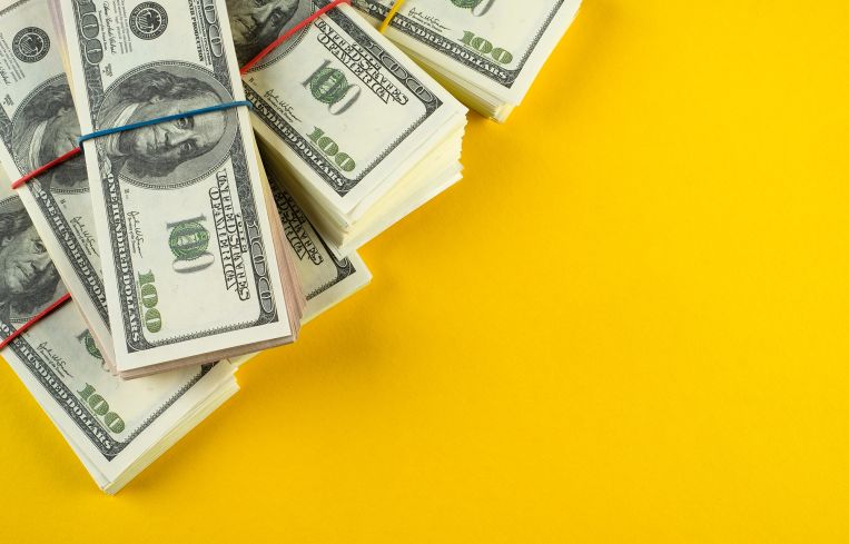 Stacks of US dollars in bundles on a bright yellow background.