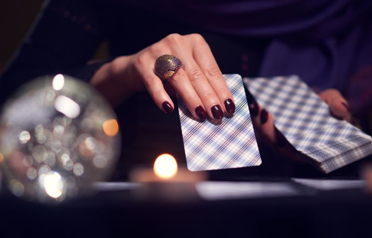 Close-up of fortuneteller's hands with cards at table with candles, magic ball in dark room, blurred background
