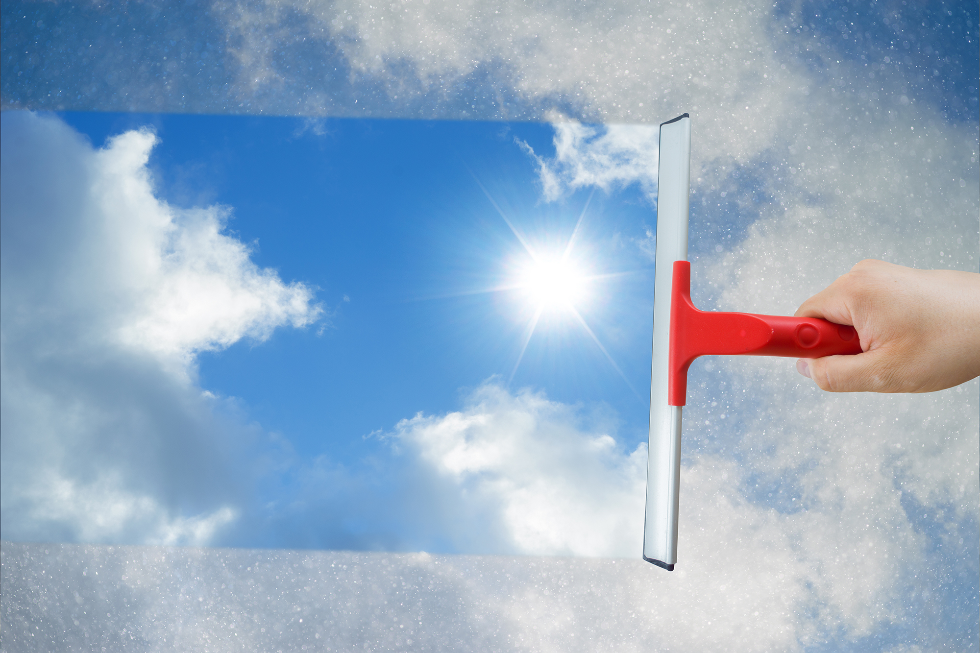 Man removing dirt from glass with a squeegee against a cloudy blue sky with sunlight.
