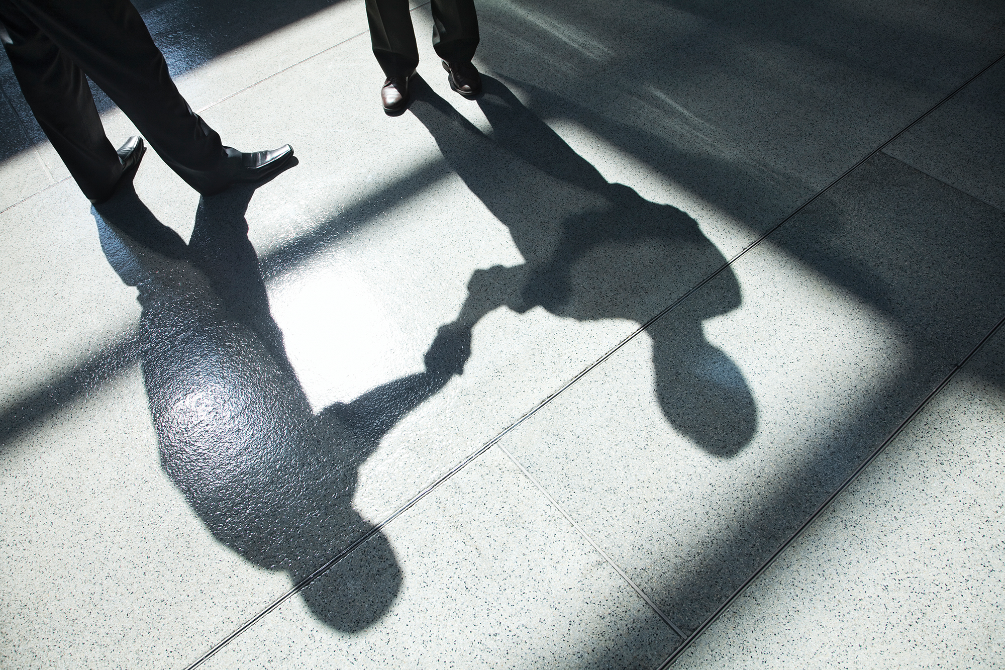 Shadows on a tiled floor of two businessmen shaking hands.