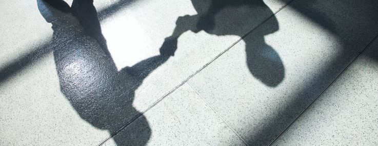 Shadows on a tiled floor of two businessmen shaking hands.