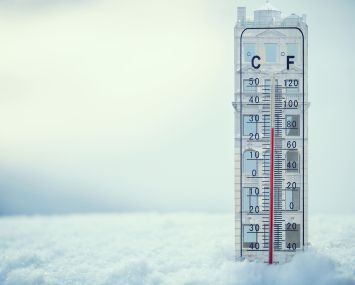 An illustration of a building shaped thermometer stuck in snow.