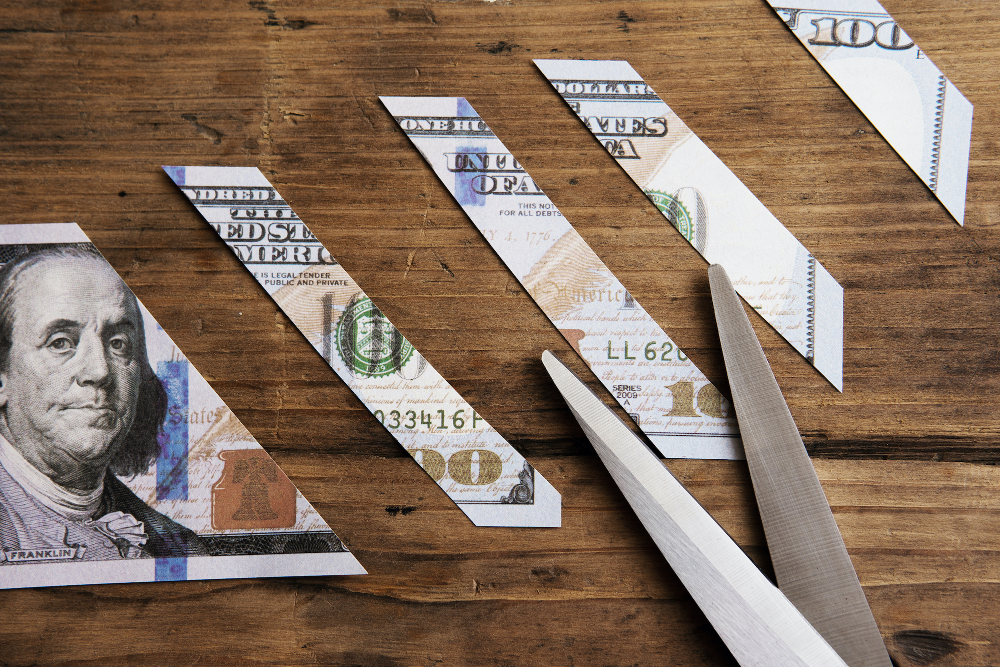 One hundred dollar bill is sliced into pieces with scissors.