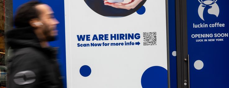 A 'Now Hiring' sign is displayed in a business's window in Manhattan.