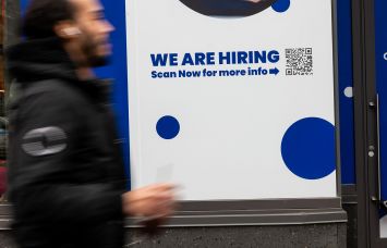 A 'Now Hiring' sign is displayed in a business's window in Manhattan.
