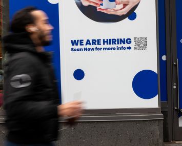A 'Now Hiring' sign is displayed in a business's window in Manhattan.