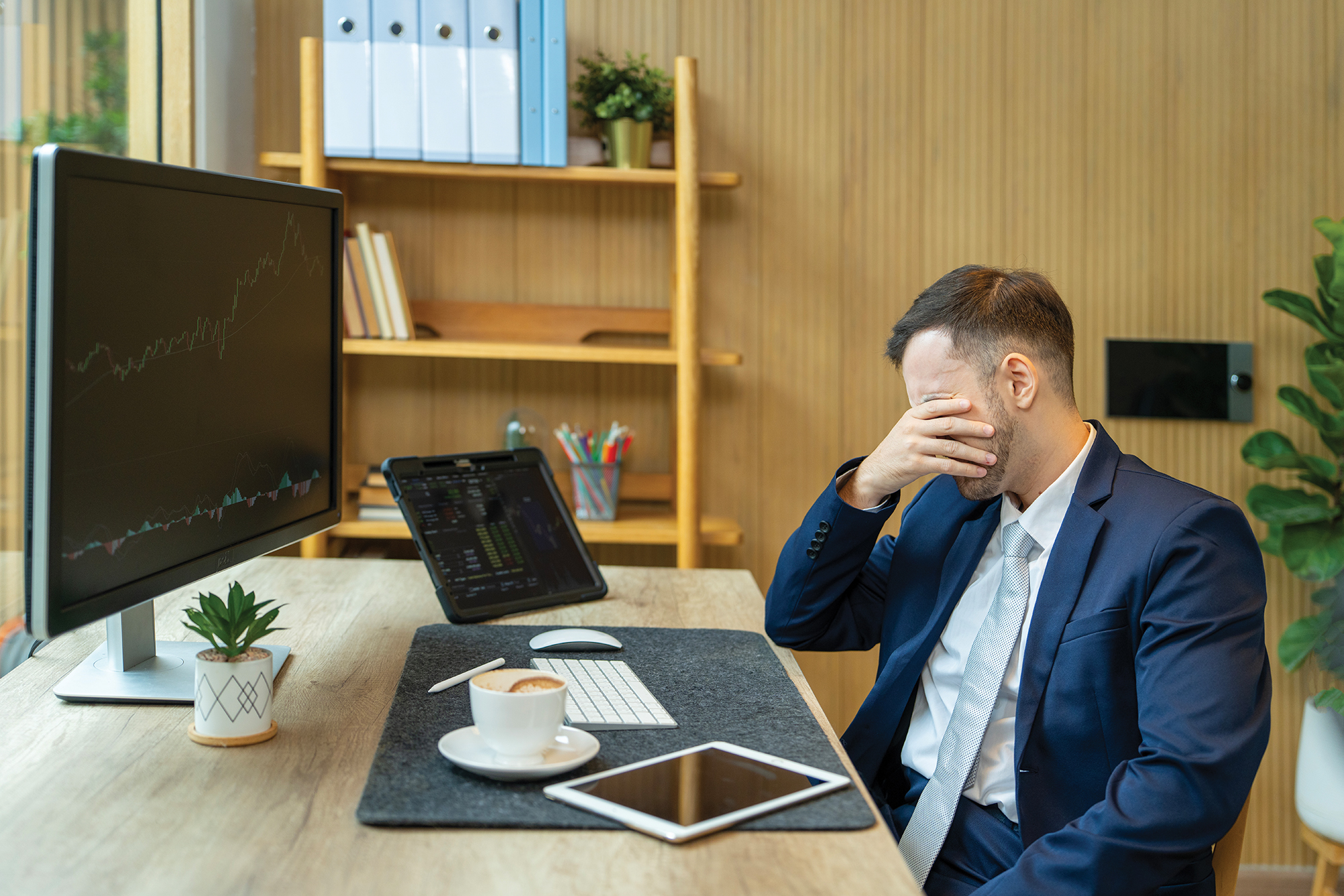 Stressed businessman covering his face with his hand while sitting at his desk.