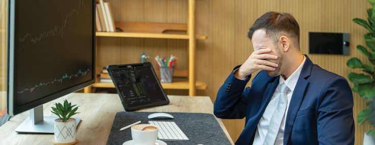 Stressed businessman covering his face with his hand while sitting at his desk.