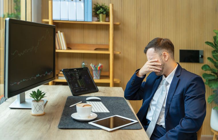 Stressed businessman covering his face with his hand while sitting at his desk.