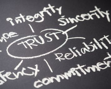 A hand writes a TRUST concept on a chalkboard.