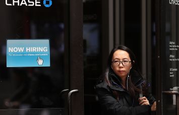 Woman walks by a "Now Hiring" sign at a Chase Bank.
