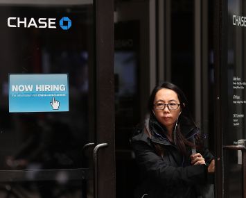 Woman walks by a "Now Hiring" sign at a Chase Bank.