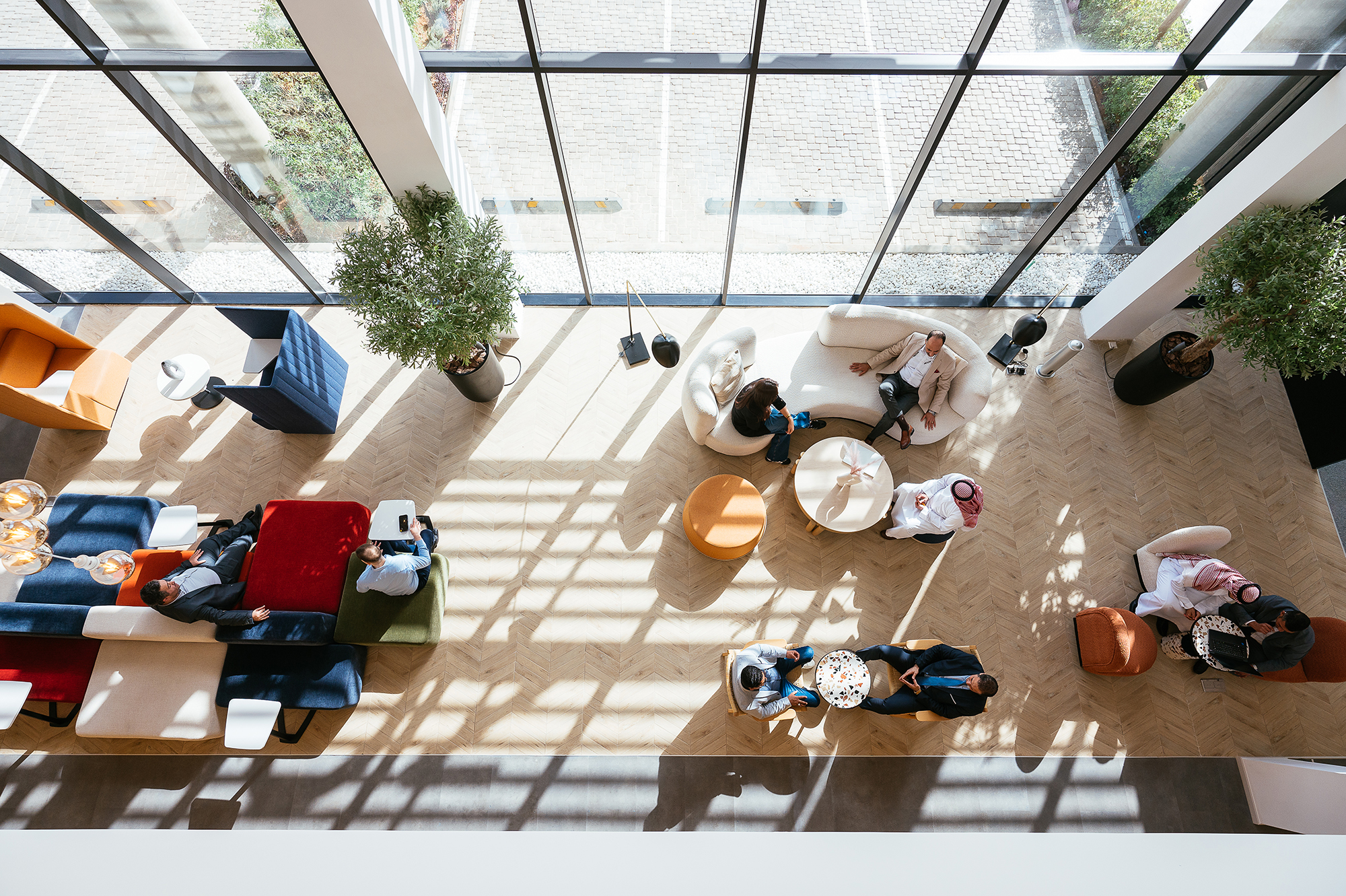 Aerial view of a modern office lounge area with diverse people interacting and natural light streaming through large windows